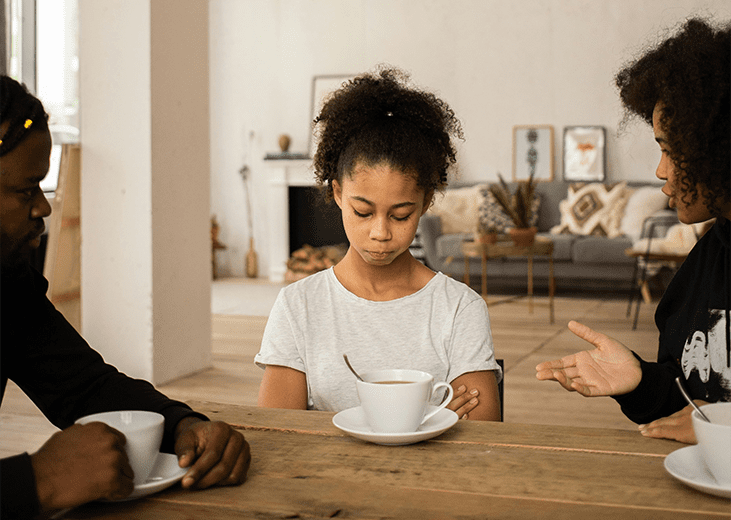 A teenager sitting at the table sad with her parents on either side talking to her. Integrea Community Mental Health System offers many services for families and children.