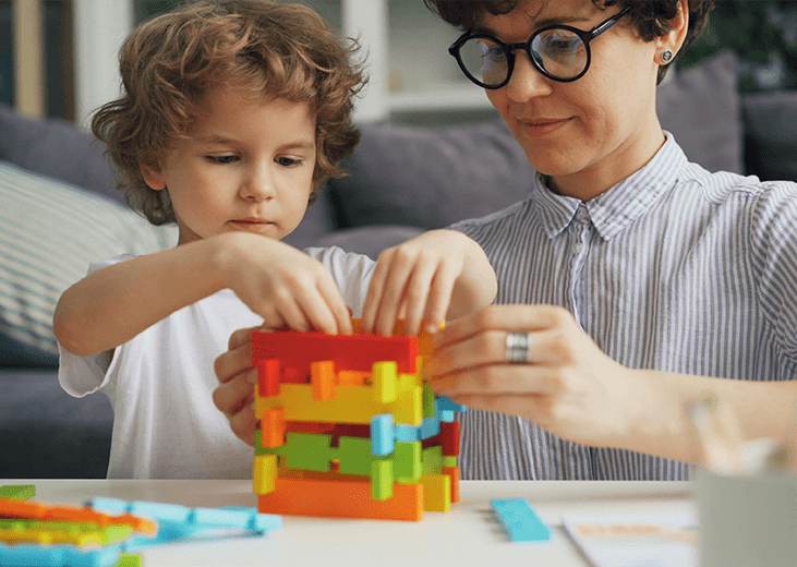 A young child playing with building block toys with the assistance of an adult. Integrea Community Mental Health System offers many services for families and children.